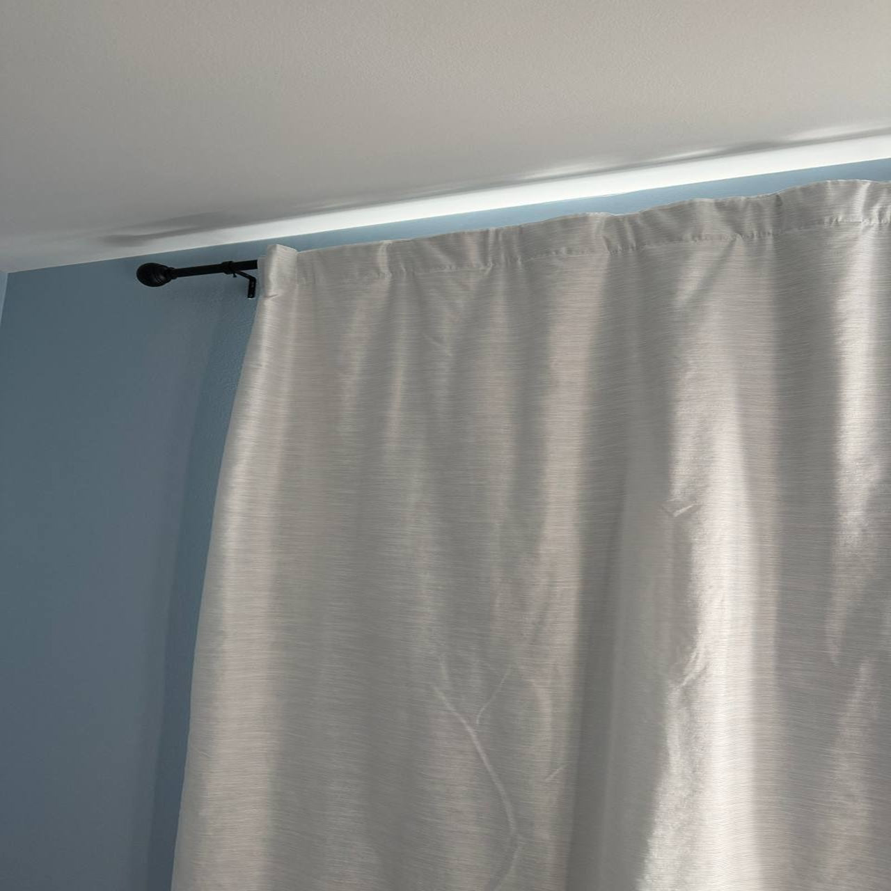 Gray curtain hanging from a rod against a light blue wall.