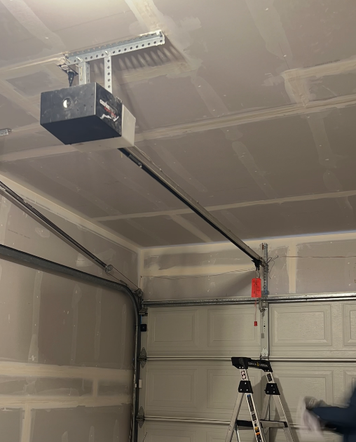 Garage door opener installation on a ceiling with a ladder in the foreground.